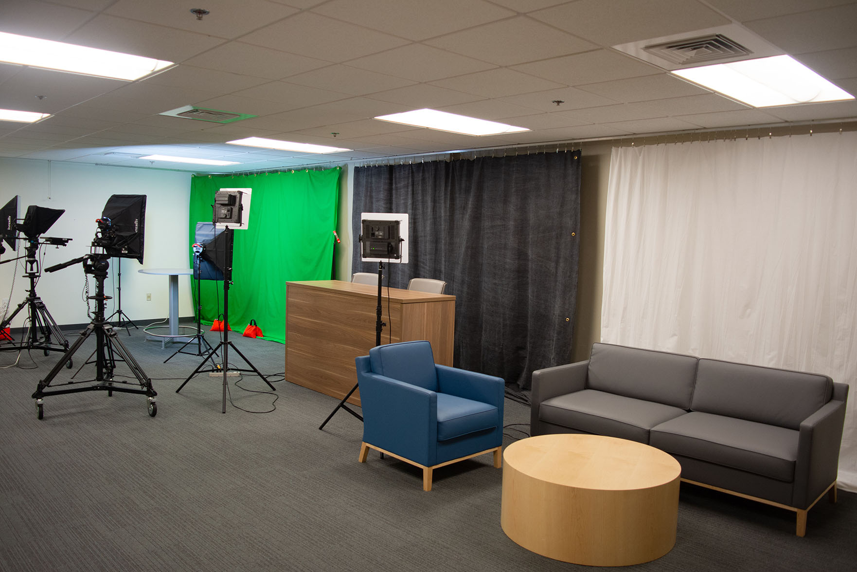 A Video Production Studio with chairs, a couch, a green screen, cameras, and lights